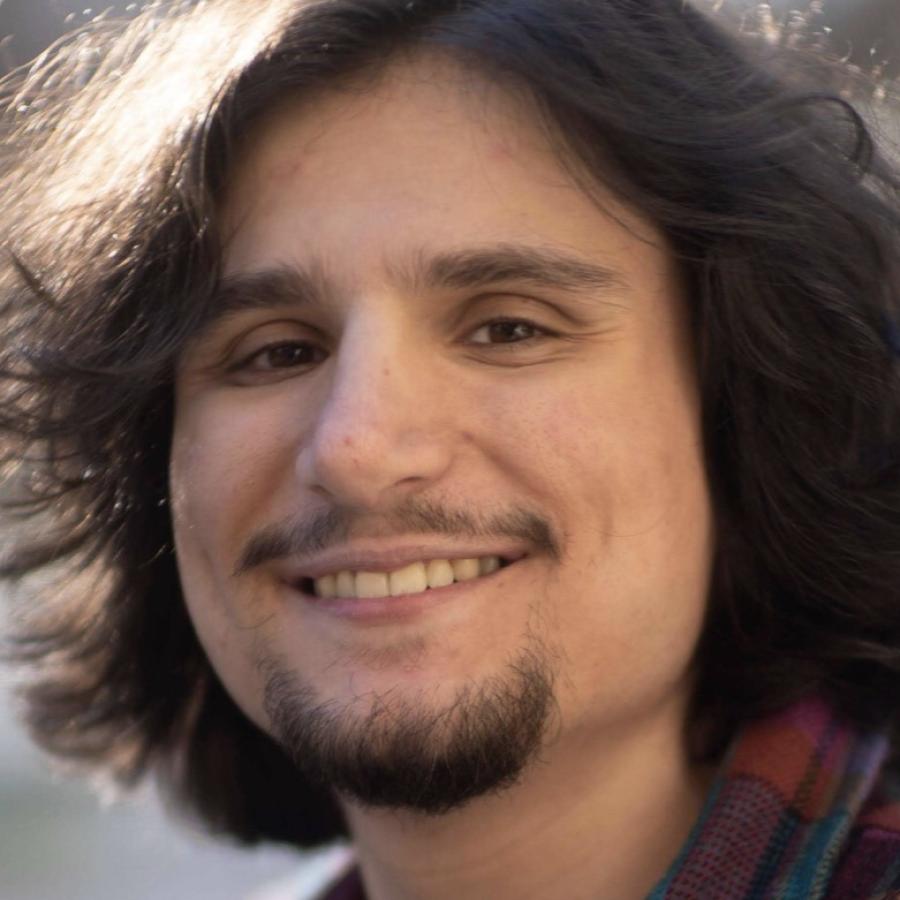 Black and white close-up photograph of a smiling young man with long dark hair and a goatee.