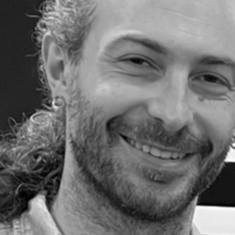 Black and white photograph of a smiling man with a beard and earring.