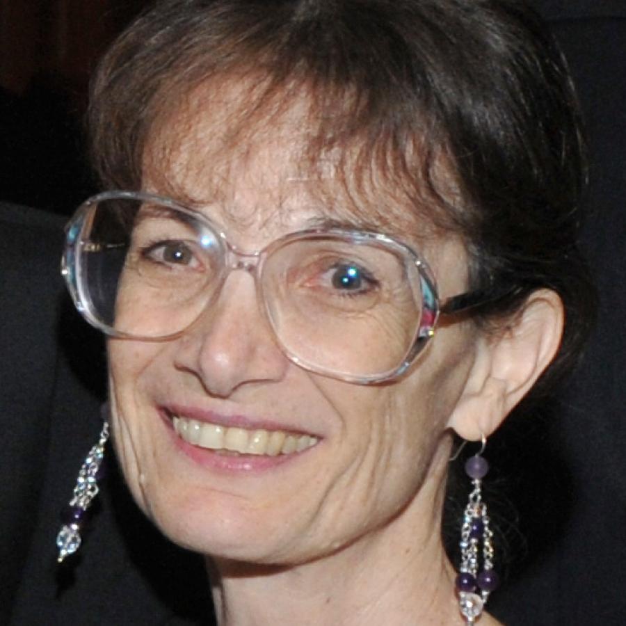 Photograph of a smiling woman wearing large glasses and dangling earrings.