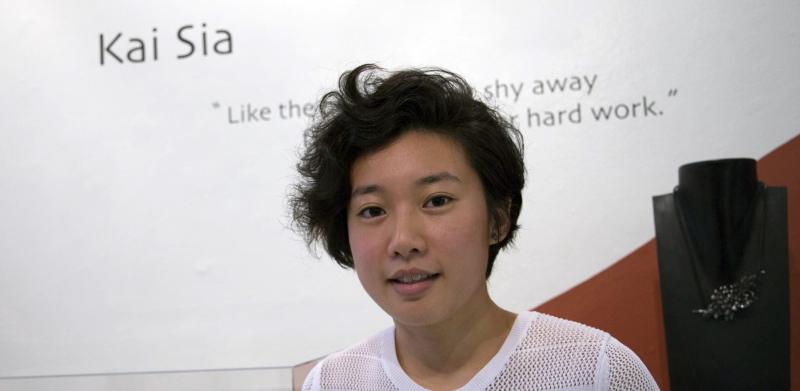 Kai standing by her work and name display