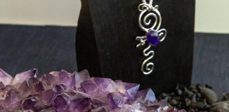 Silver necklace with purple gem on stand, amethyst cluster.