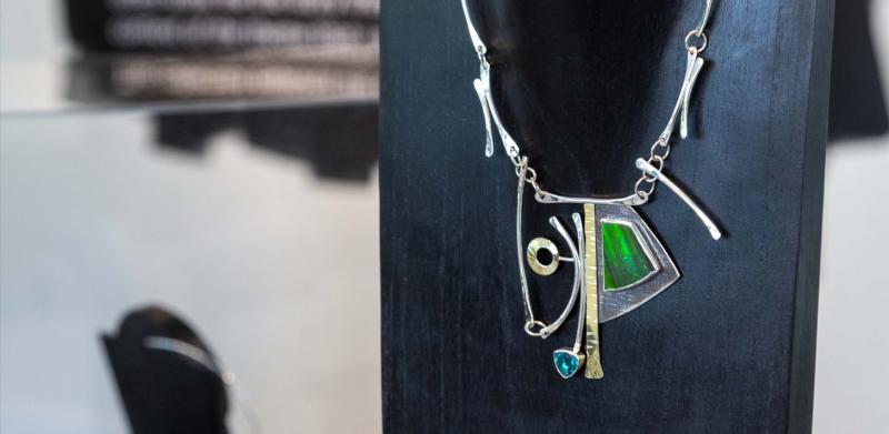Photograph of a sculptural silver and green pendant necklace on a black mannequin display.