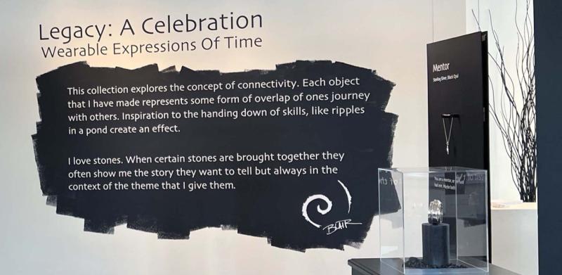 A gallery display titled "Legacy: A Celebration" featuring jewelry on black stands.