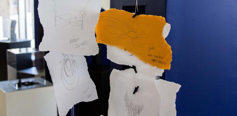 Hand-drawn sketches on paper hanging by clips in a gallery space.