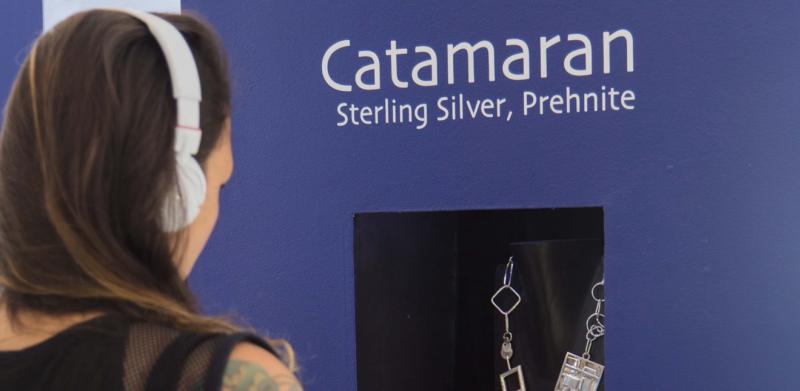 A woman wearing headphones looks at a necklace in a display case at an exhibit.