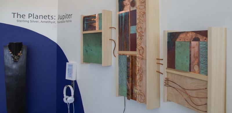 A gallery wall featuring three abstract wooden art pieces with metal panels and an adjacent necklace.