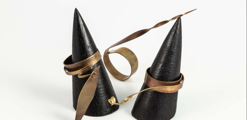 Unusual copper rings displayed on black conical stands against a white background.