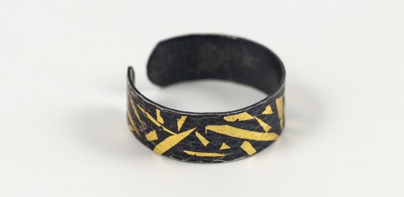 Black metal bracelet with an open back and jagged gold inlay on a white background.