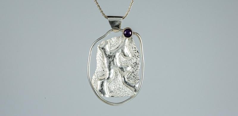 A photograph of a silver pendant with a small amethyst on a delicate silver chain.