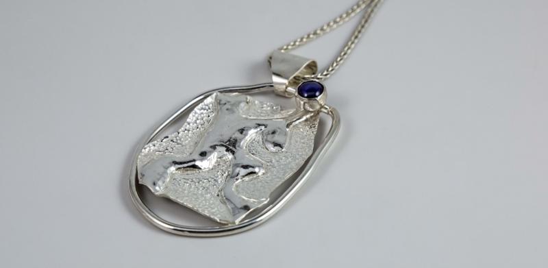 Photograph of a textured silver pendant with a small purple stone on a silver chain.