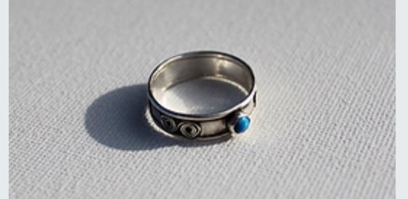 Silver ring with a small blue gemstone on a textured white surface.