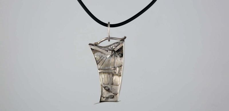 Photograph of a textured, asymmetric silver pendant on a black cord.