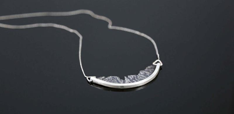 Silver crescent-shaped pendant necklace on a dark background.