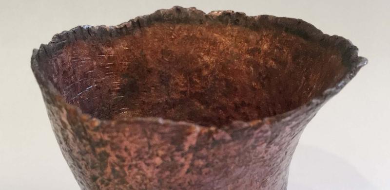 Photograph of a small, textured copper-colored bowl with an organic, uneven rim.