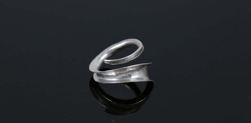 Photograph of a curved, silver-toned metal ring on a black reflective surface.