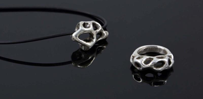 Photograph of a silver organic-patterned pendant necklace and matching ring on a dark surface.