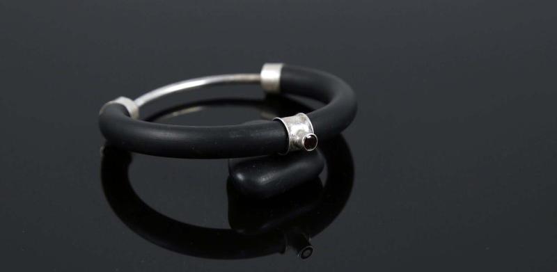 A black rubber and silver bangle bracelet reflected on a dark, glossy surface.