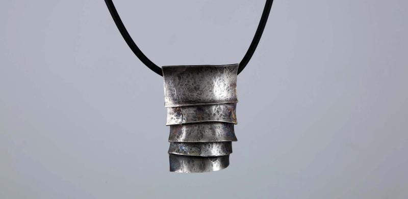 Photograph of a layered, textured silver pendant on a black cord.
