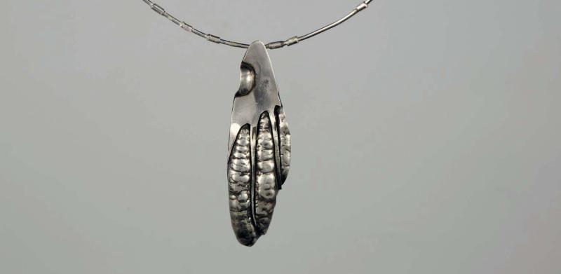 Photograph of a silver pendant shaped like a textured, stylized claw on a thin chain.