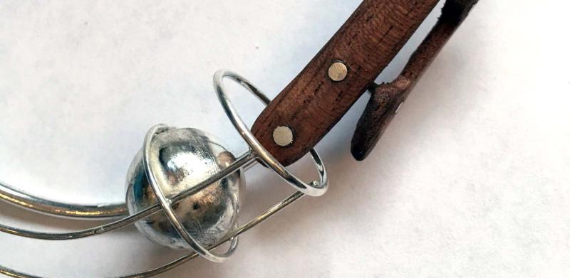 Photograph of a silver wire neckpiece with a dark wooden clasp detail and a metallic sphere.