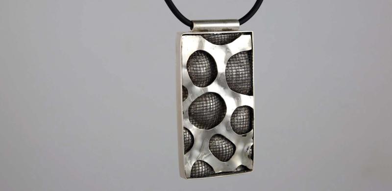 Rectangular silver pendant with a textured, porous pattern on a black cord necklace.