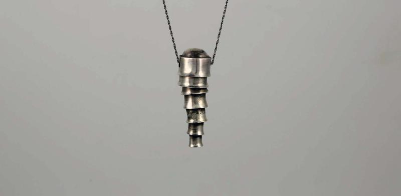 Photograph of a tapered silver pendant hanging from a thin dark string.
