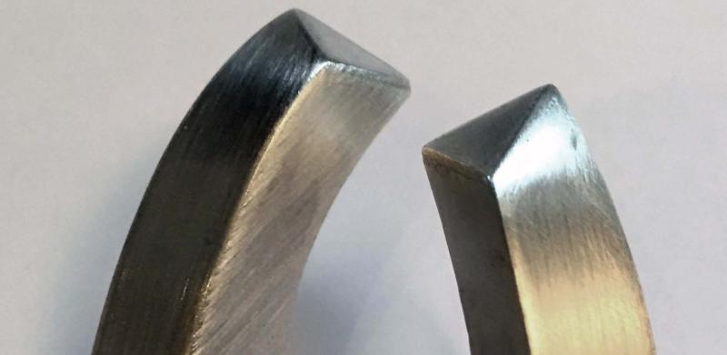 Photograph of two curved, brushed metal components against a plain white background.
