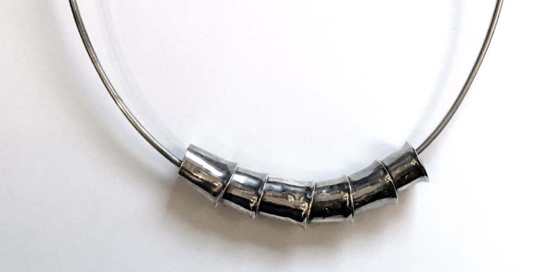 A silver open-ended neck collar featuring five cylindrical metal beads.