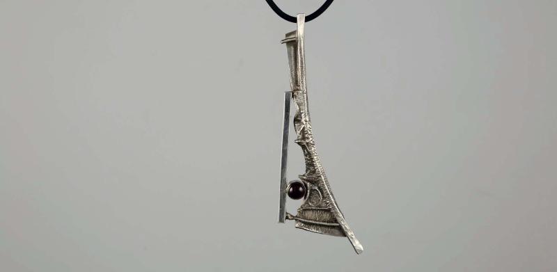 Photograph of an abstract silver pendant with a small dark gem on a black cord.