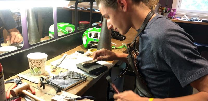 A young artisan focuses on crafting jewelry at a cluttered workbench.