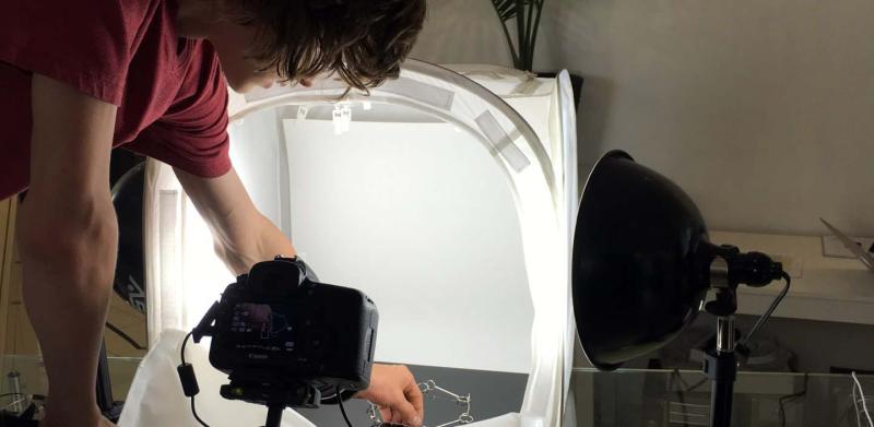 Photographer arranging a small object inside a lit tabletop photography studio.