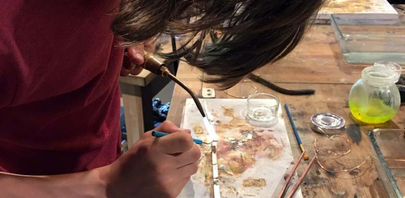 A person wearing a maroon shirt soldering a piece of metal on a wooden workbench.