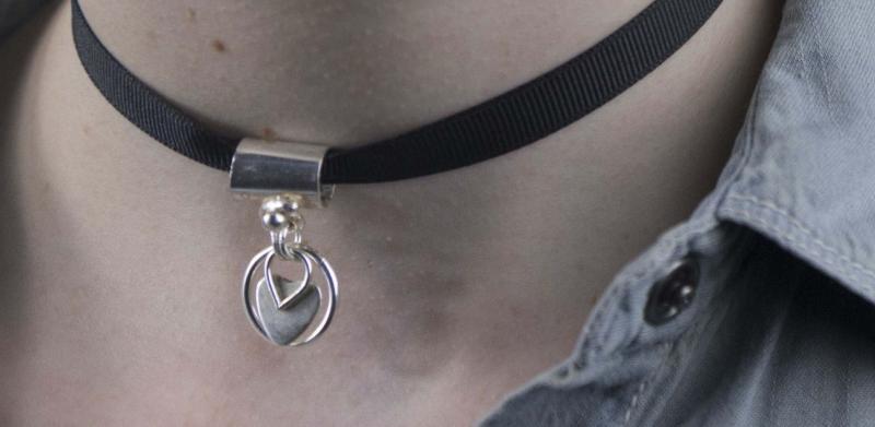 A person with blue hair wears a black ribbon choker with a silver charm and a small earring.