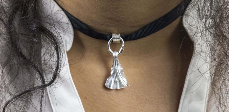 Photograph of a person wearing a black ribbon choker with a silver pendant.