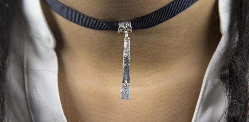 A person wearing a black ribbon choker necklace with a silver vertical pendant.