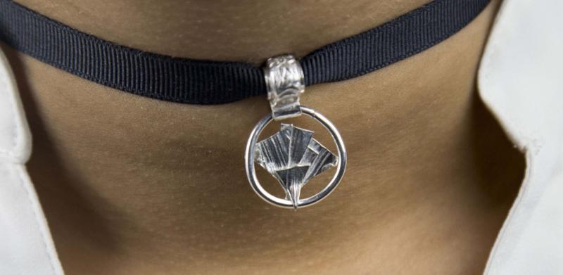Close-up of a black fabric choker with a circular silver pendant.