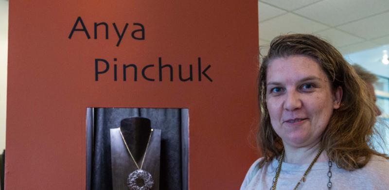 A woman standing next to a display with the name "Anya Pinchuk" on an orange wall.