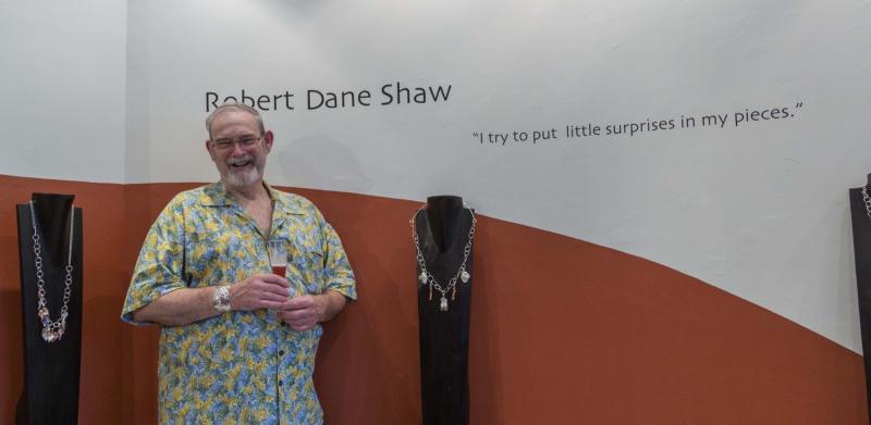 Photograph of a smiling man in a yellow shirt standing next to jewelry displays.
