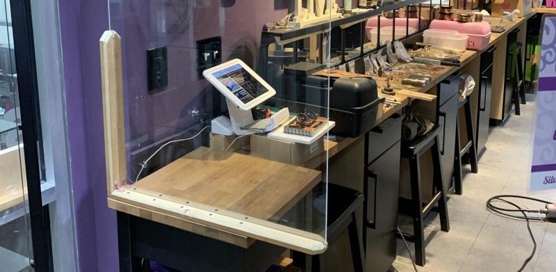 Interior photograph of a jewelry store featuring a clear acrylic protective barrier on a checkout desk.