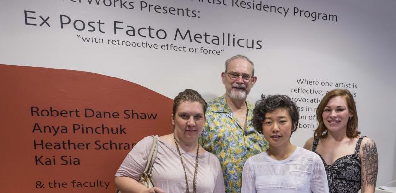 Photograph of four smiling artists in front of exhibition wall text.