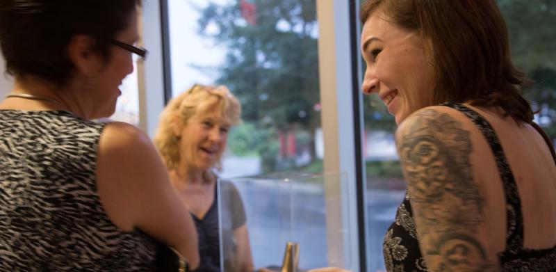 Photo of three women smiling while looking at a display case.