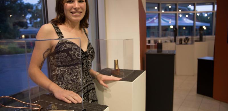 Photograph of a woman smiling beside glass display pedestals in an art gallery.