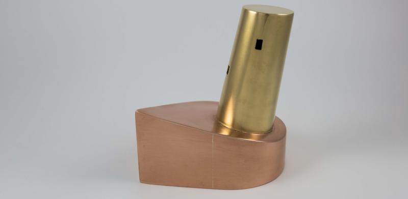 A small sculpture made of a copper base and a tilted brass cylinder.