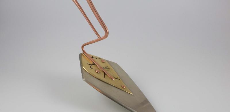 A modern cake server with a copper loop handle and a triangular blade.