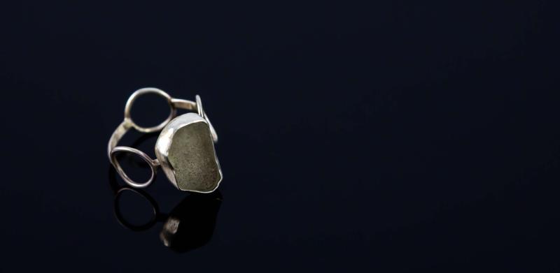 Photograph of a silver ring with a stone on a black background.