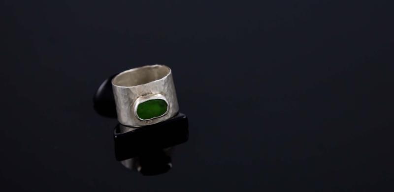 Photograph of a silver ring with a green stone on a black surface.