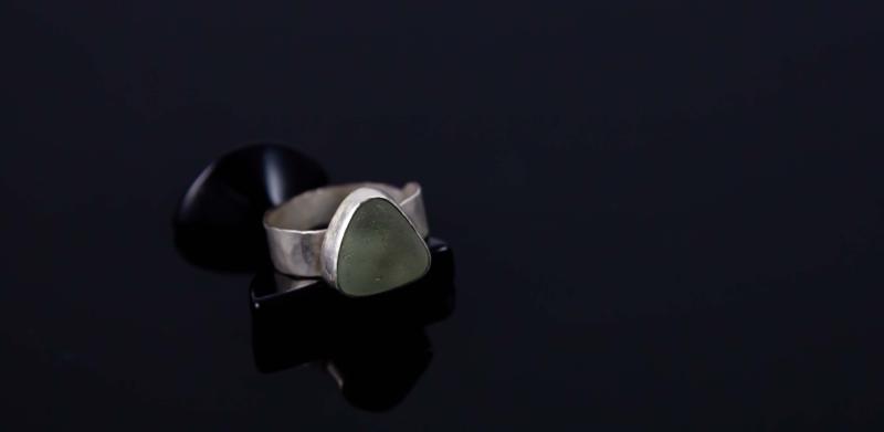 Photograph of a silver ring with a pale green stone on a black surface.