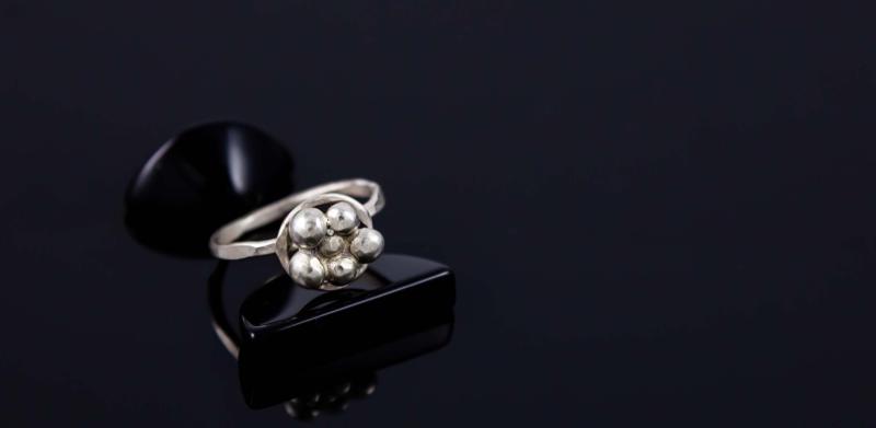 A silver ring with cluster beads sits on a black reflective surface against a dark background.