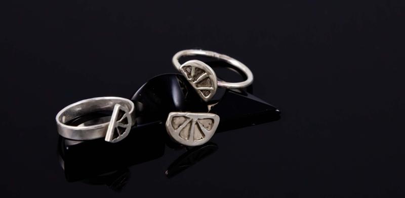 A photograph of two silver rings with citrus-slice motifs resting on a black surface.