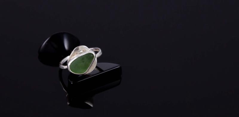 Photograph of a silver ring with a green sea glass stone on a black surface.